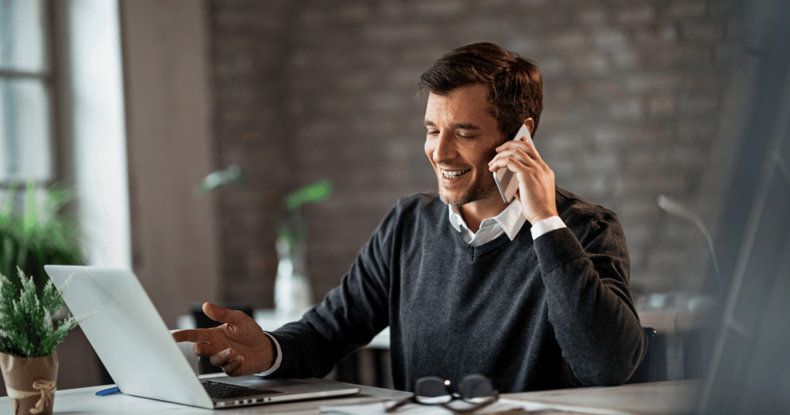 Man sitting at desk on the phone and using his laptop